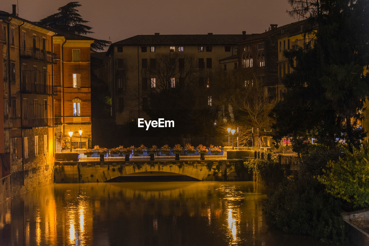 Illuminated bridge over canal by buildings in city at night