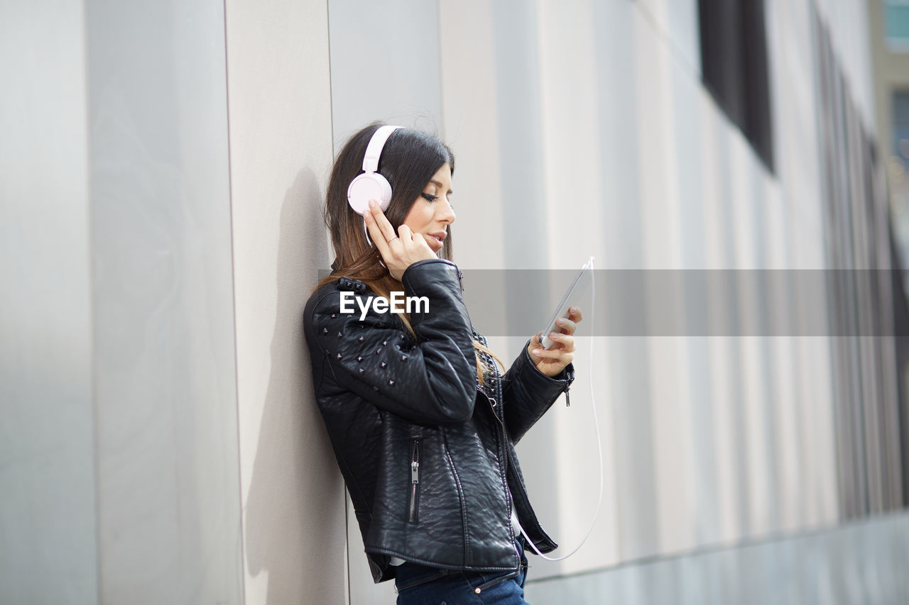 Young woman using mobile phone while standing against wall