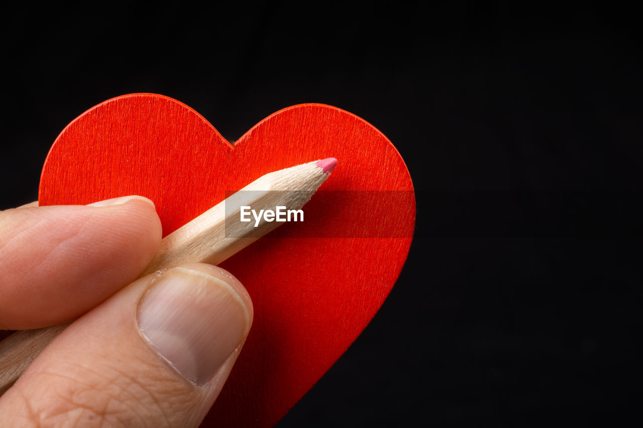 CLOSE-UP OF PERSON HOLDING HEART SHAPE OVER BLACK BACKGROUND