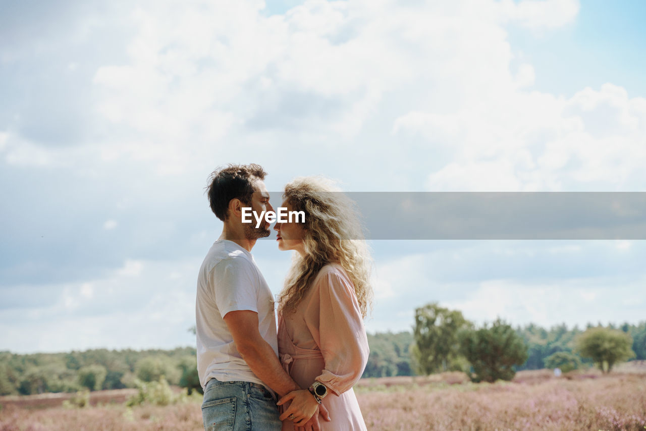 Side view of couple standing on field against sky and looking to each other