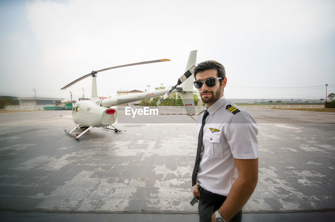 VIEW OF MAN STANDING BY AIRPLANE ON AIRPORT RUNWAY