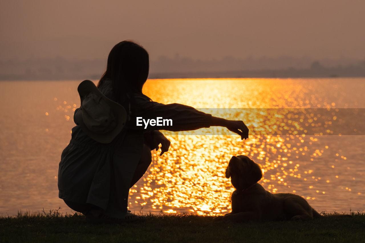 sunset, sky, silhouette, nature, water, sunlight, adult, land, sea, beach, beauty in nature, evening, one person, orange color, sitting, men, horizon, lifestyles, sun, outdoors, leisure activity, emotion, dusk, relaxation, person, positive emotion, women, backlighting, animal