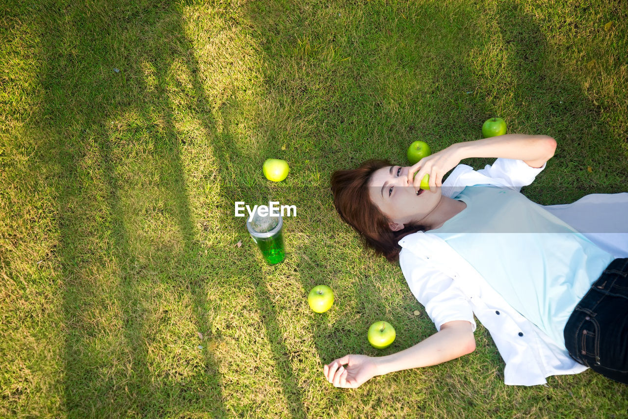 High angle portrait of woman eating apple while lying on grass