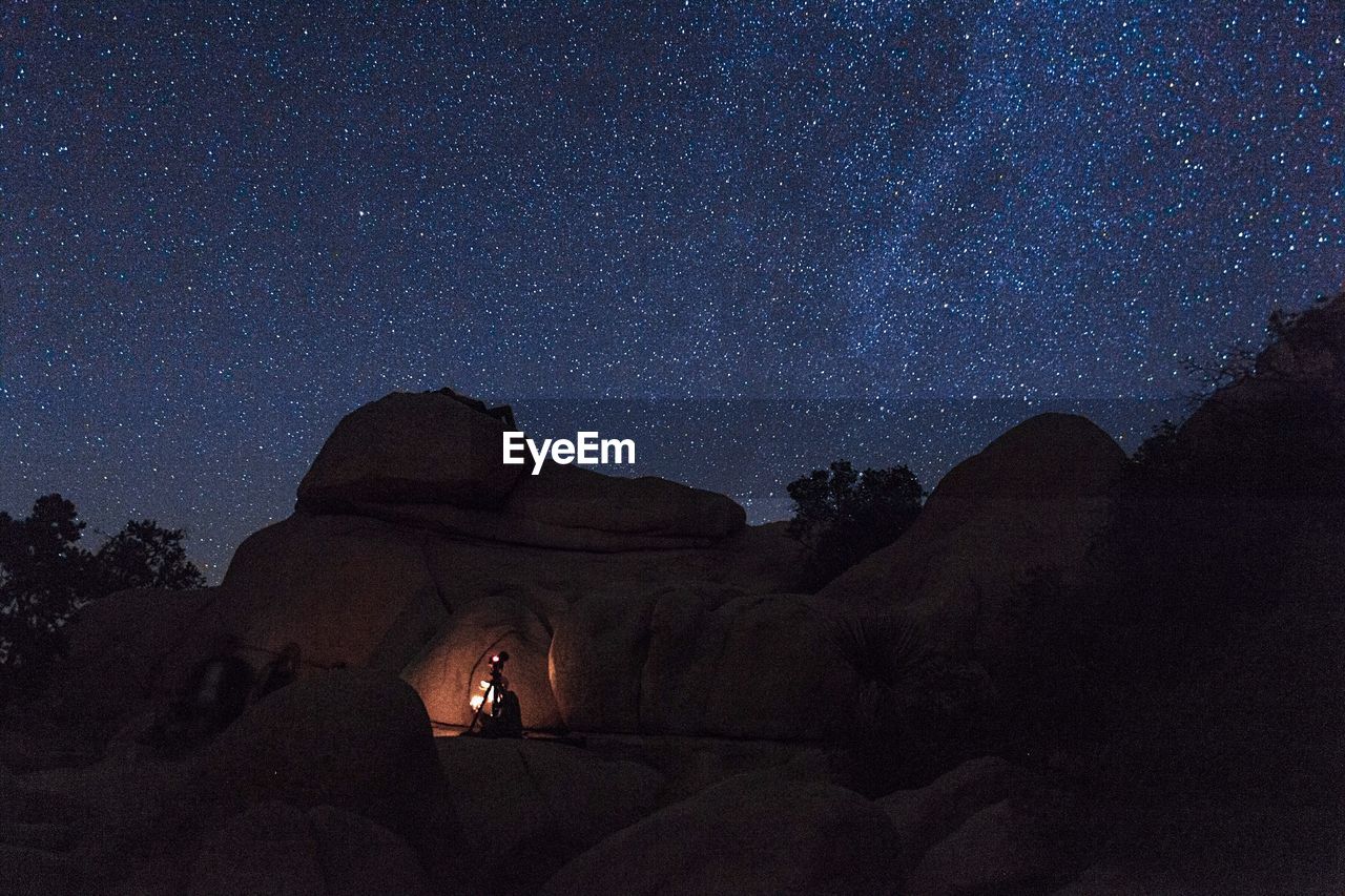 Silhouette of photographer on rocks against sky at night