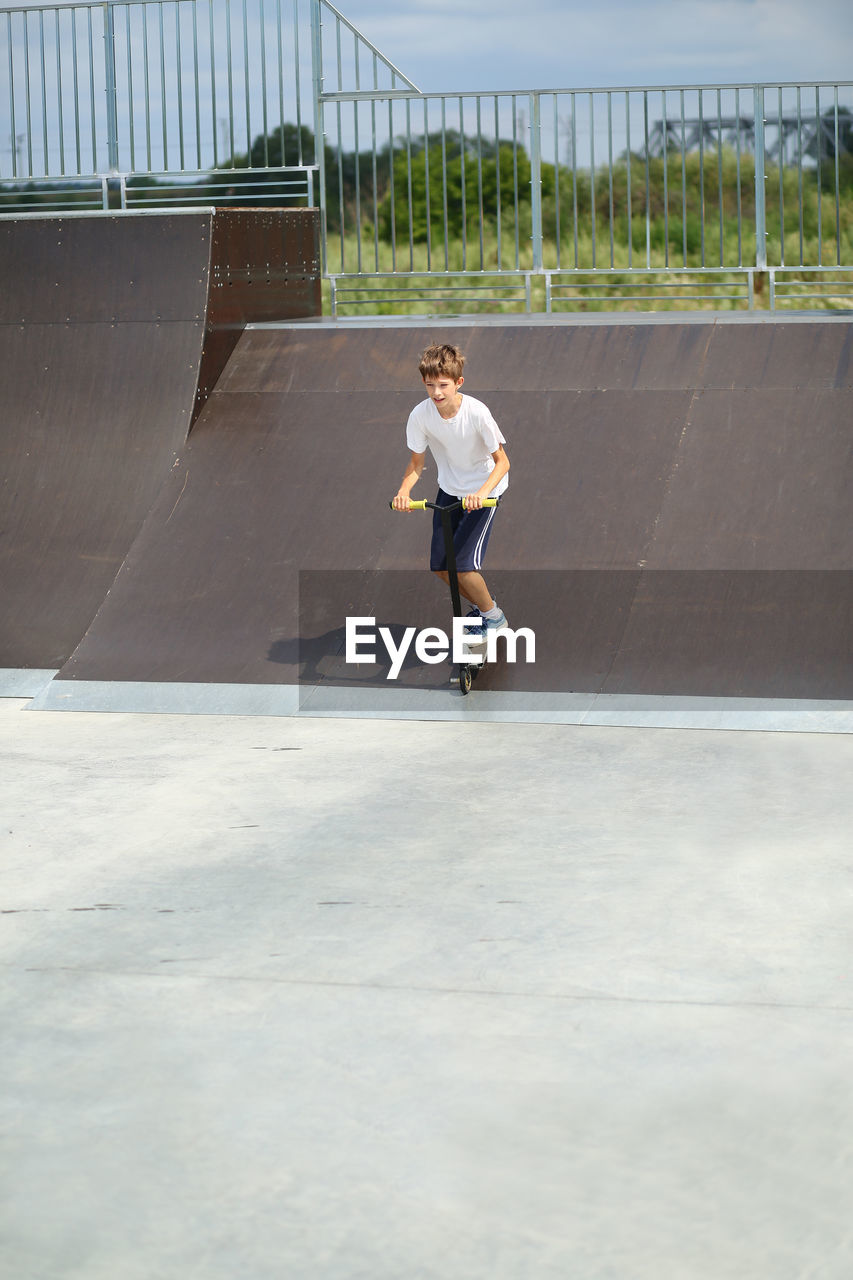 Active ten year old boy riding a scooter in the summer skate park