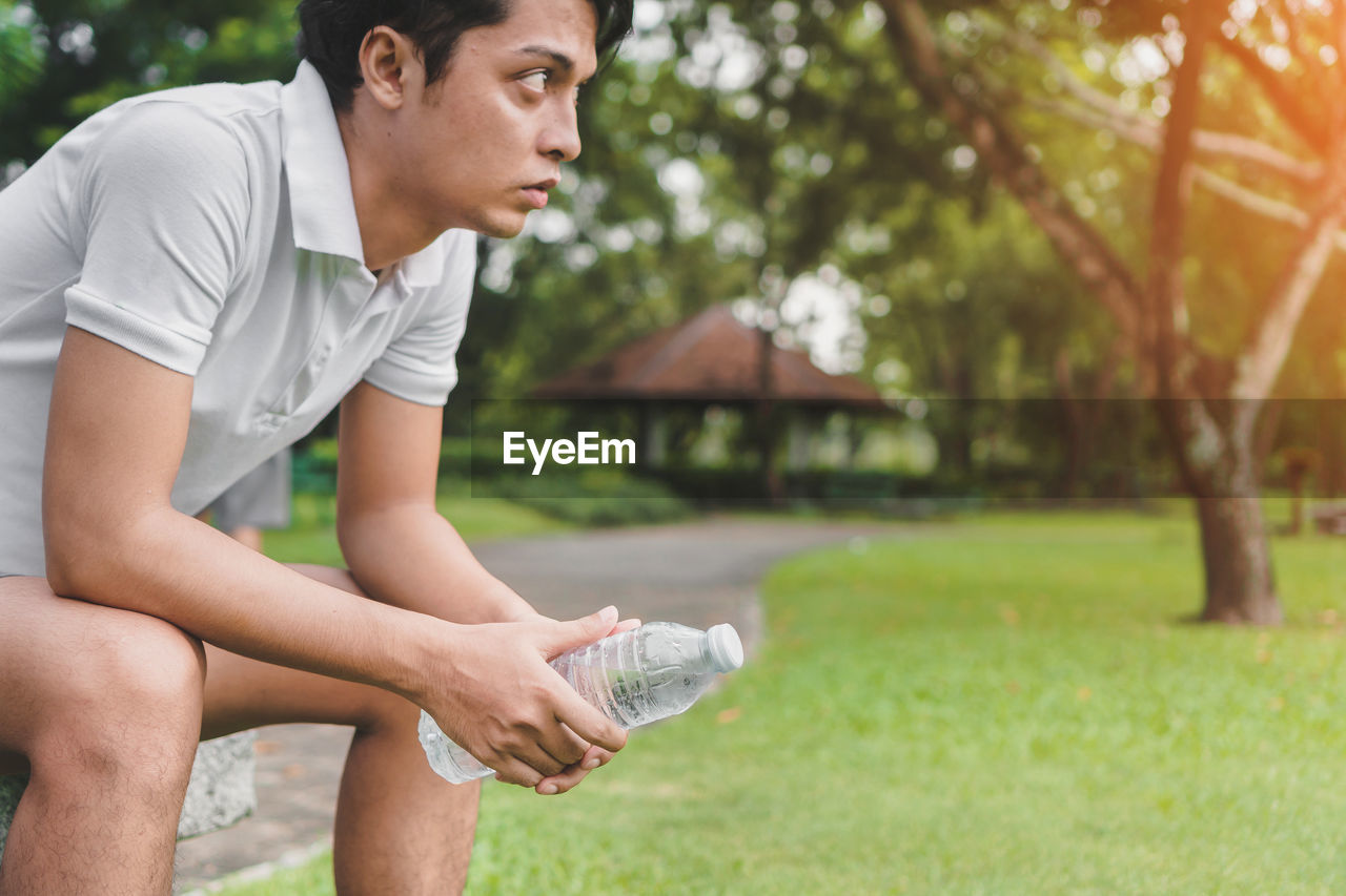 Young man holding water bottle while sitting in park