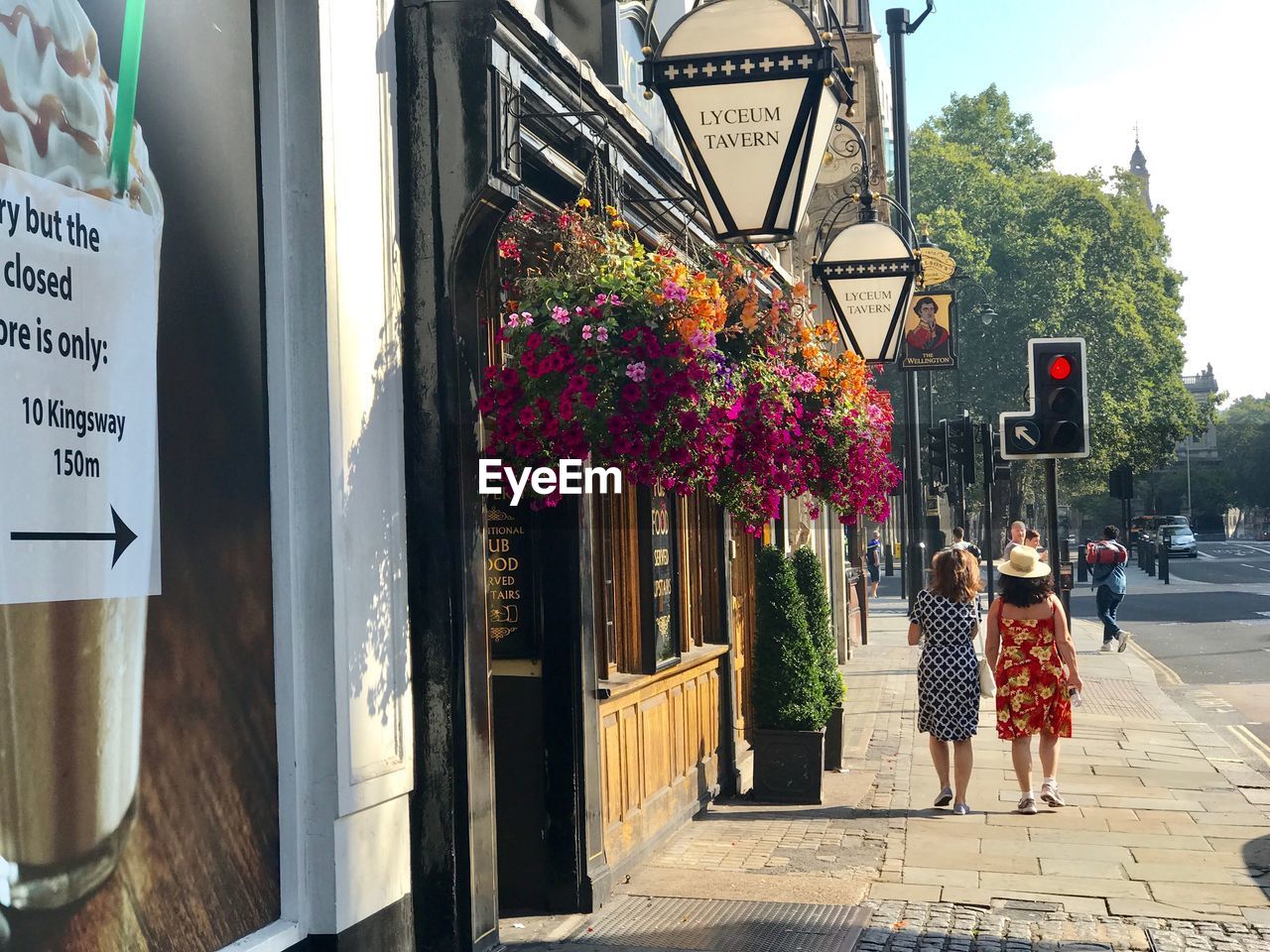 REAR VIEW OF PEOPLE WALKING ON FOOTPATH BY STREET