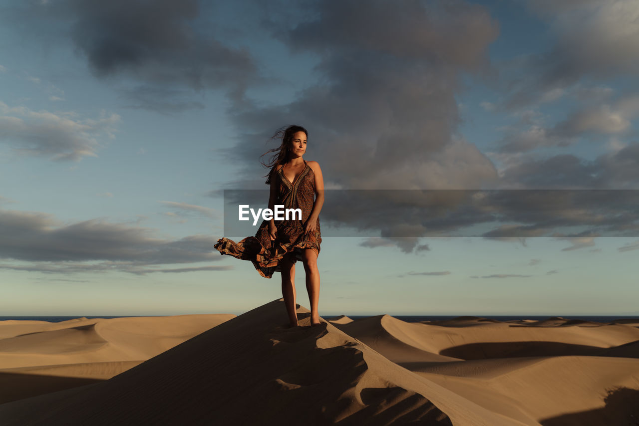 Woman standing on sand dune by sea against sky