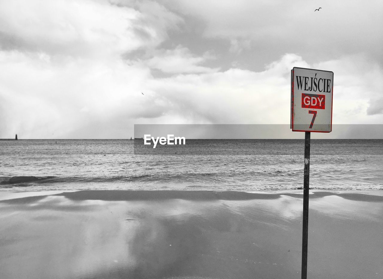 WARNING SIGN ON SEA SHORE AGAINST CLOUDY SKY