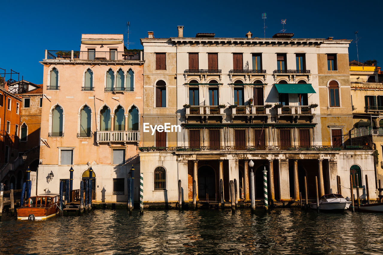 Buildings by canal against clear sky in city