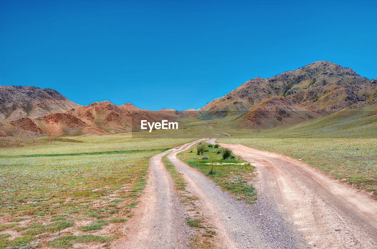 Dirt road amidst landscape against clear blue sky