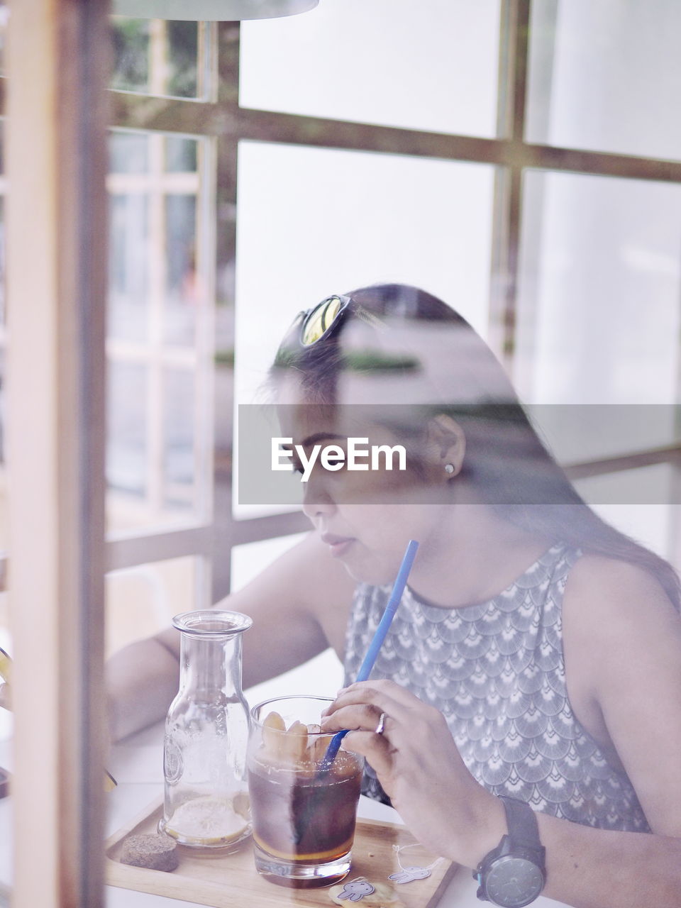 Woman having drink at cafe seen through glass window