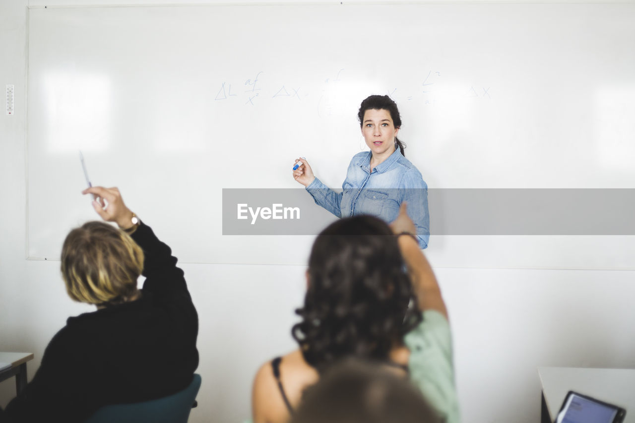 Students pointing at teacher standing against whiteboard in classroom