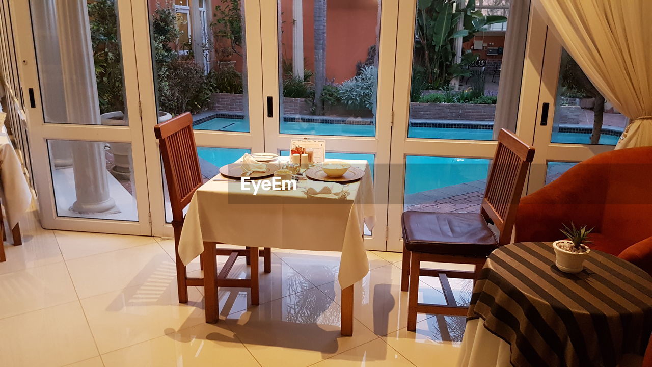 EMPTY CHAIRS AND TABLES IN SWIMMING POOL AGAINST WINDOW