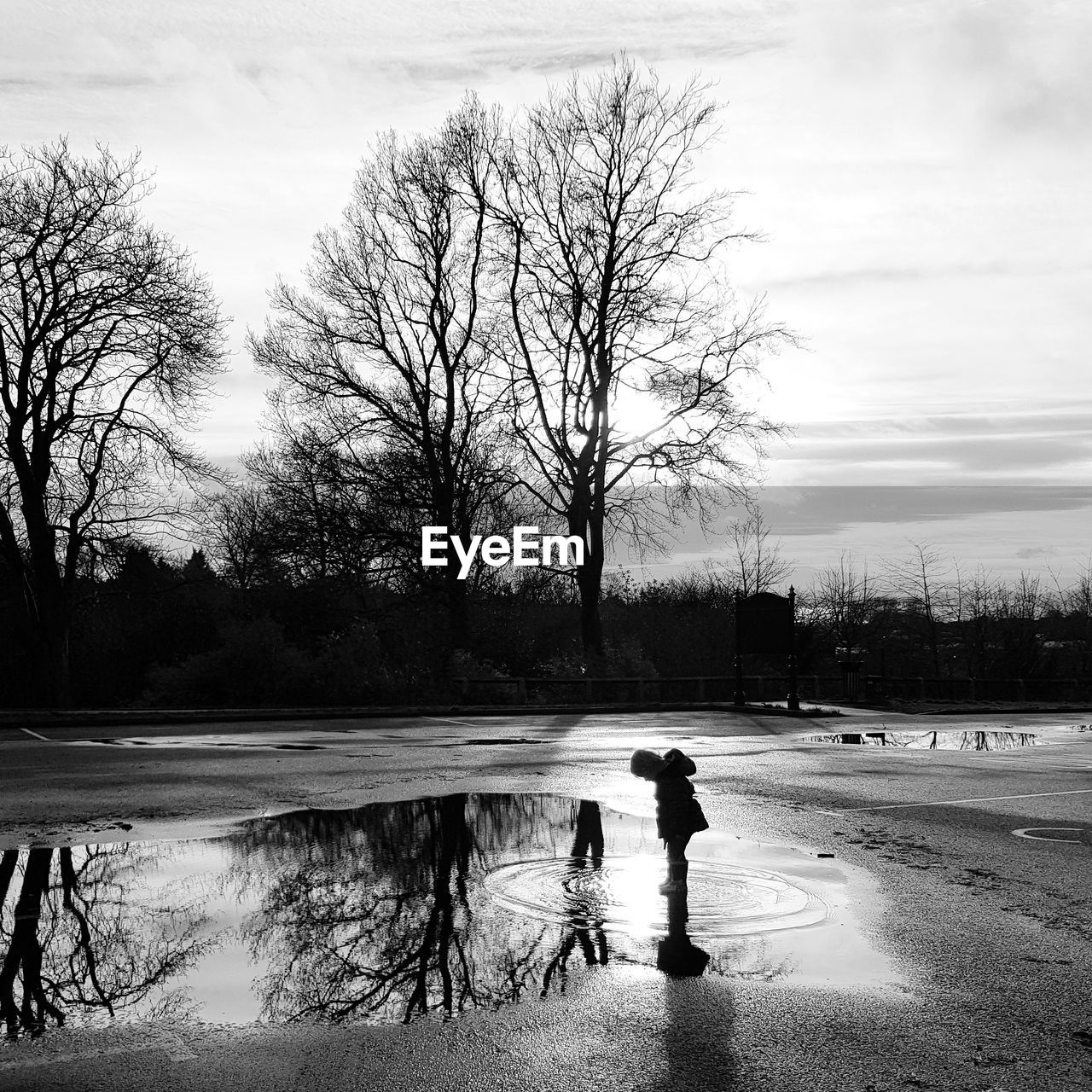 Girl standing in puddle against bare trees