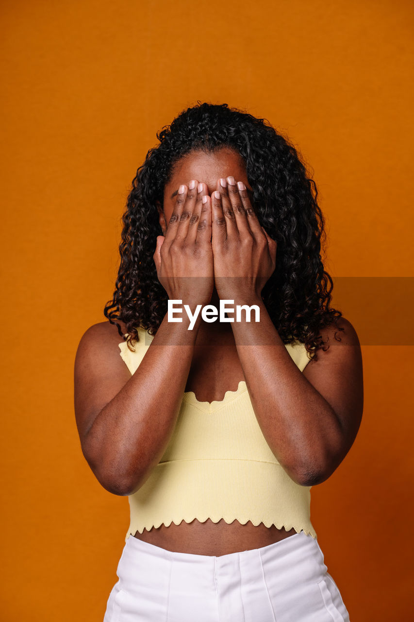 rear view of young woman standing against yellow background