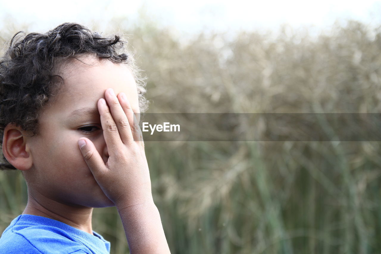 Close-up of boy covering face while standing against plants