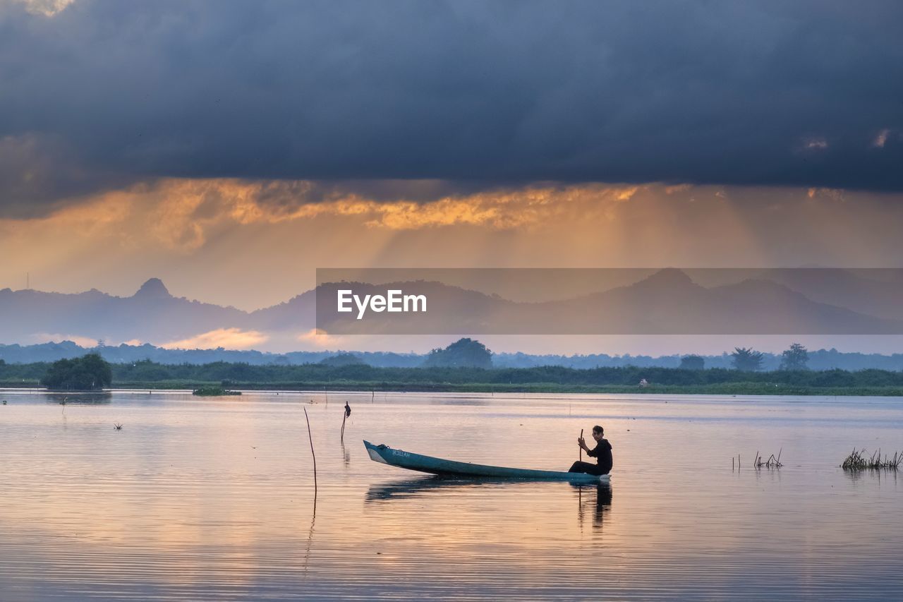 Man on boat in lake against sky during sunset