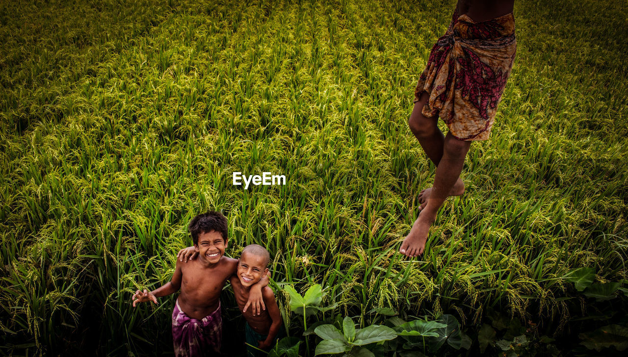 REAR VIEW OF PEOPLE STANDING ON FIELD BY PLANTS