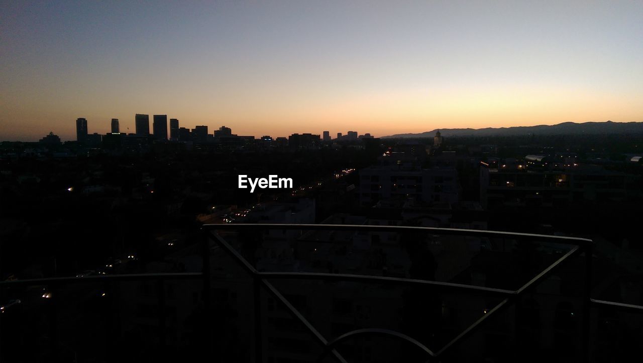 Silhouette city seen through observation point against clear sky during sunset