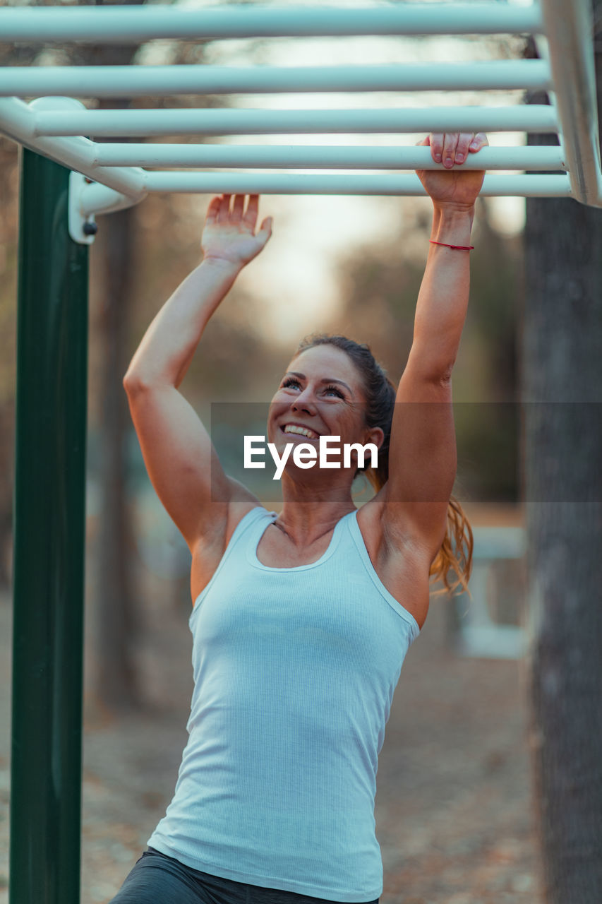 Smiling woman exercising on monkey bars in park