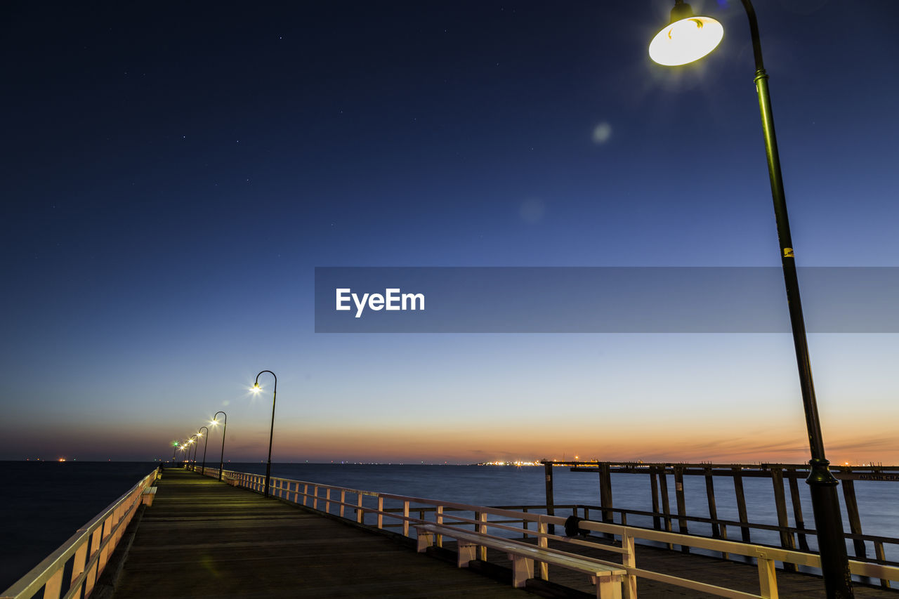 Illuminated pier over sea against sky during sunset