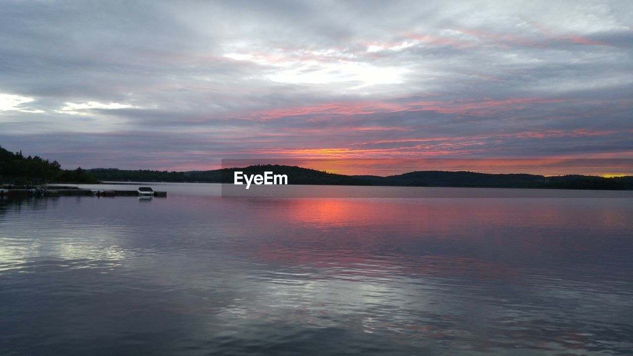 Scenic view of lake against cloudy sky at sunset