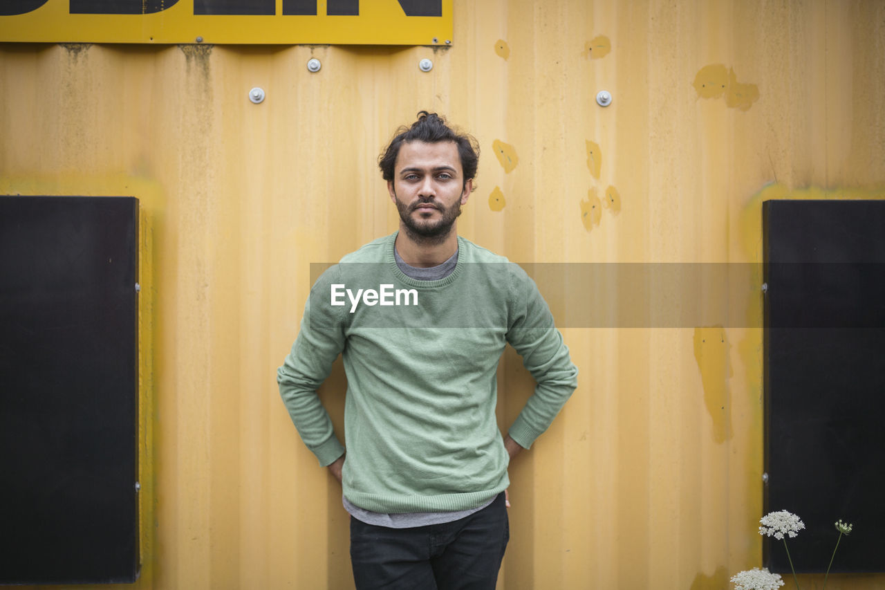 PORTRAIT OF SMILING YOUNG MAN STANDING AGAINST YELLOW WALL