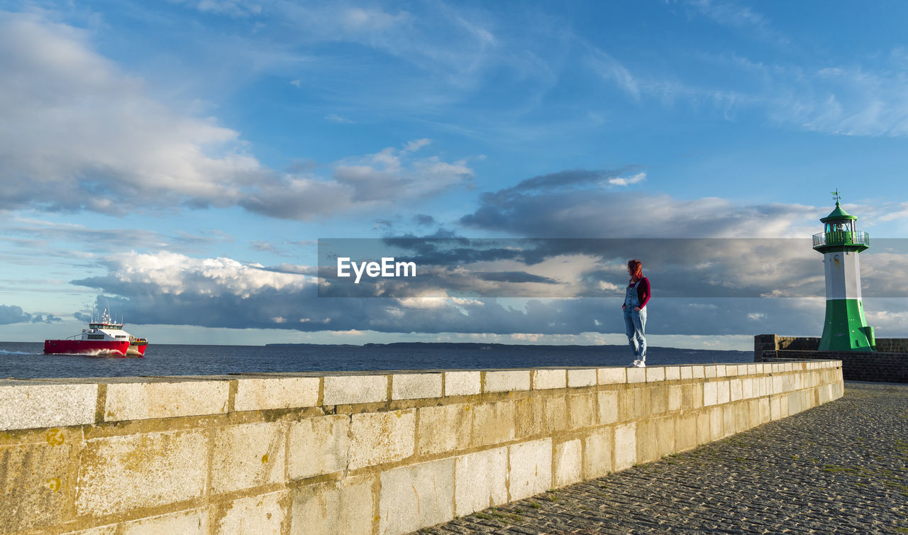 MAN STANDING ON RETAINING WALL AGAINST SEA