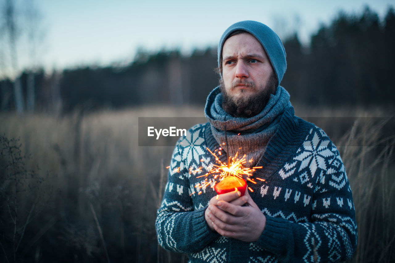 Thoughtful man holding sparkler while standing on field