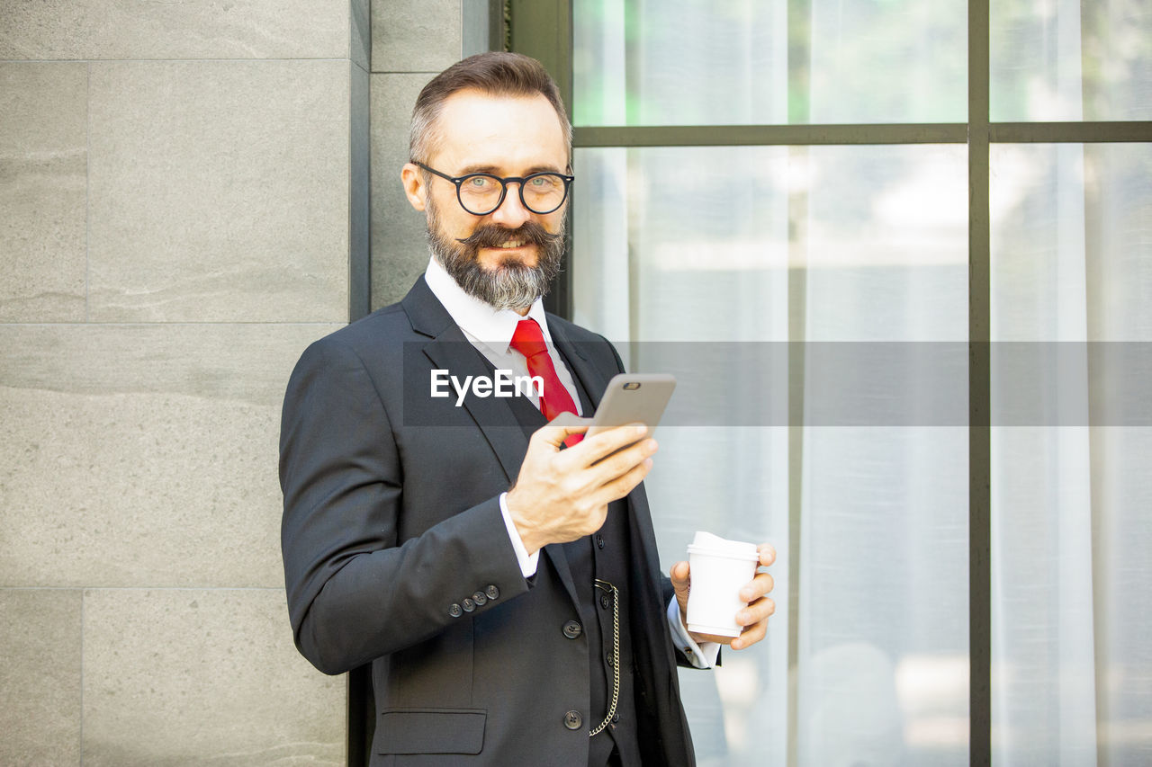 Smiling businessman using smart phone while sitting outdoors