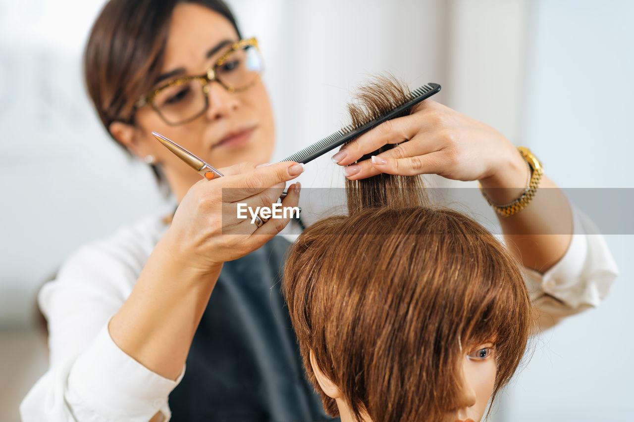 Hairdresser educator with students, explaining hair cutting technique on mannequin head for training