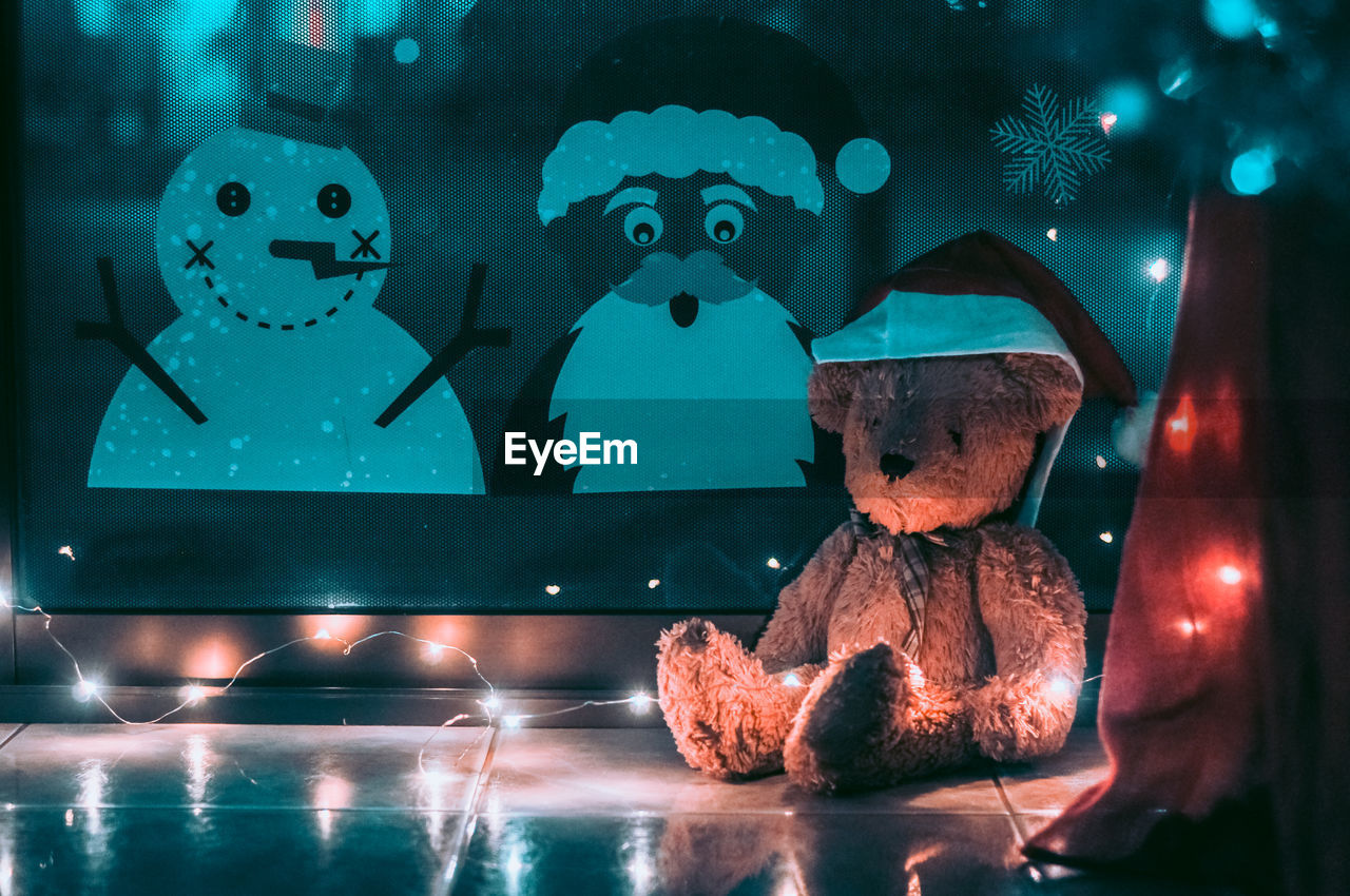 Teddy bear with santa hat and illuminated string lights in room