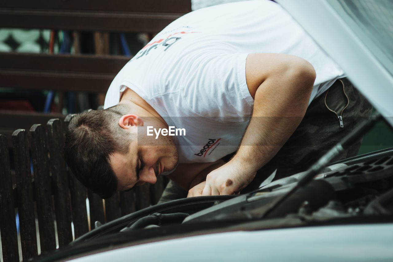 PORTRAIT OF MAN SLEEPING BY CAR