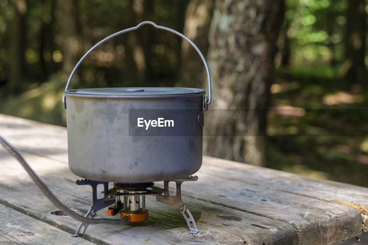 A titanium pot for making food on a gas stove on a camping wooden table in the forest.