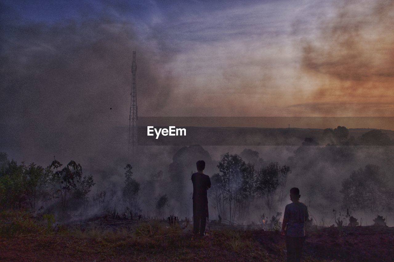 cloud, morning, fog, sky, nature, smoke, environment, men, mist, land, silhouette, outdoors, adult, burning, wildfire, two people, standing, fire, dawn, landscape, plant, accidents and disasters