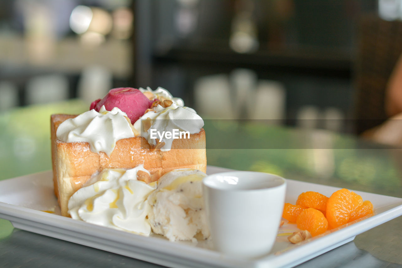 Honey toast with red homemade ice cream and whipping cream topping serve with orange.