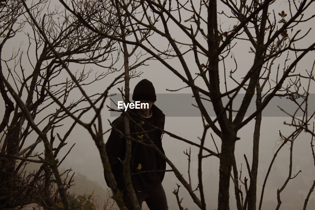 Man standing by bare tree during winter