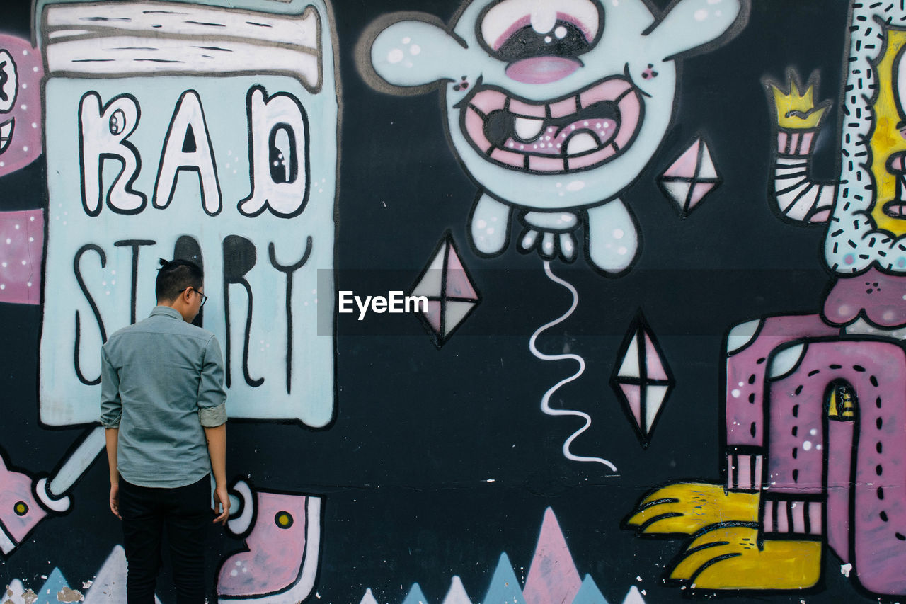 Rear view of man against graffiti on wall