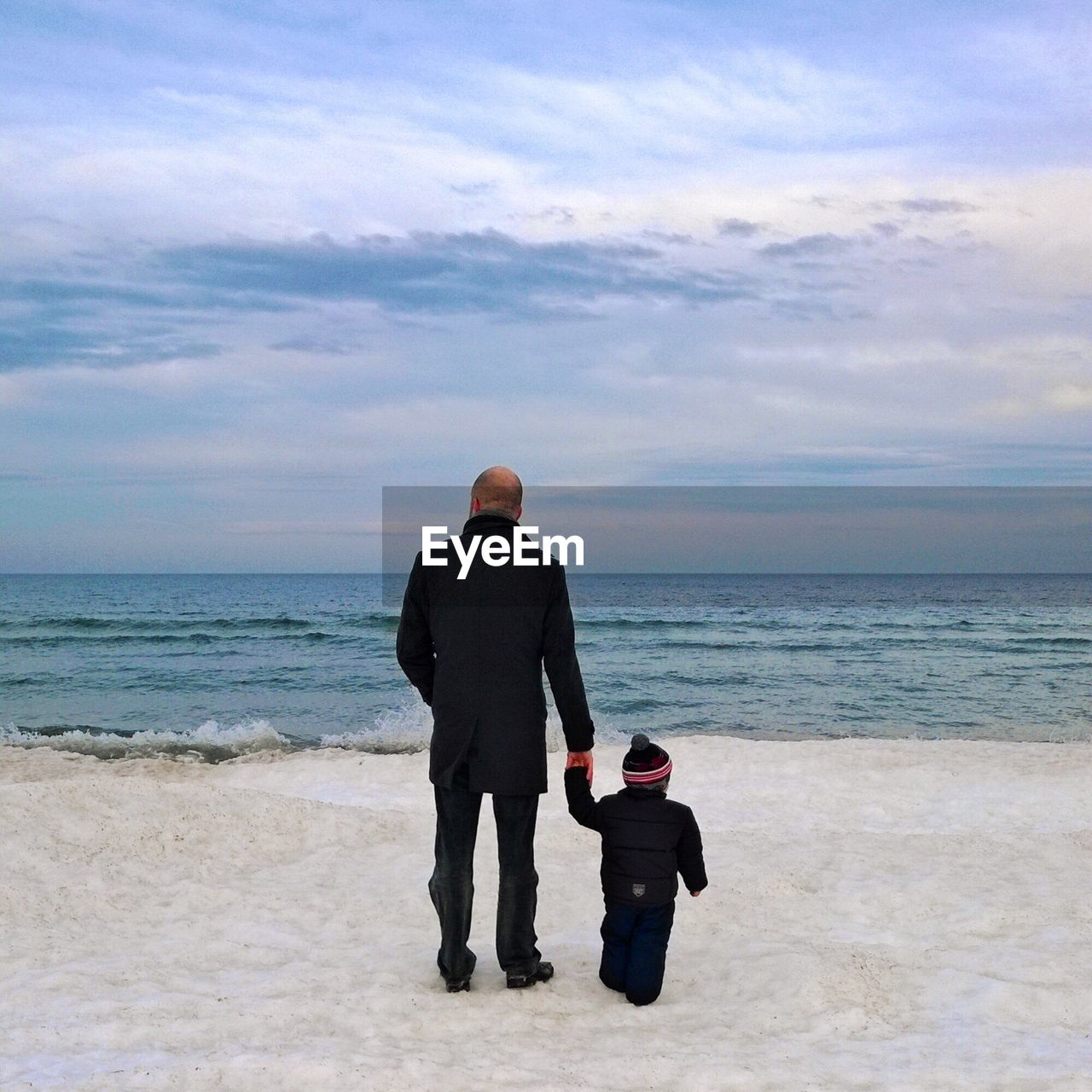 Rear view of man  and toddler standing on beach in winter