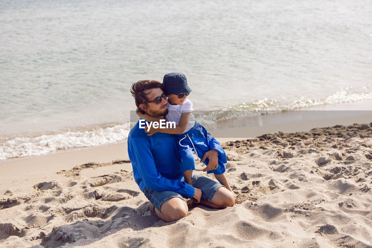 Dad and son play on the beach in summer in blue clothes while on vacation