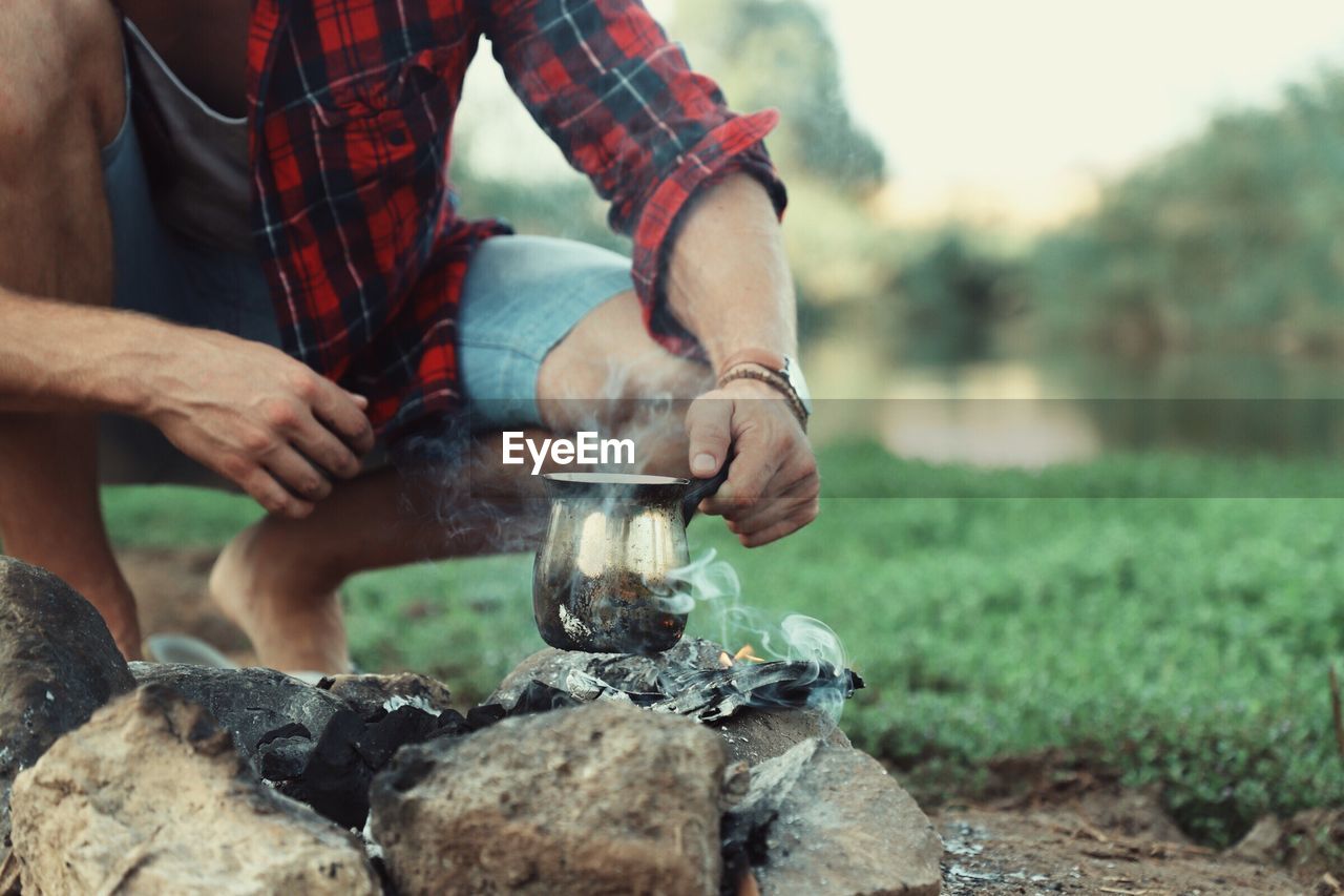 Midsection of man boiling drinking water on campfire