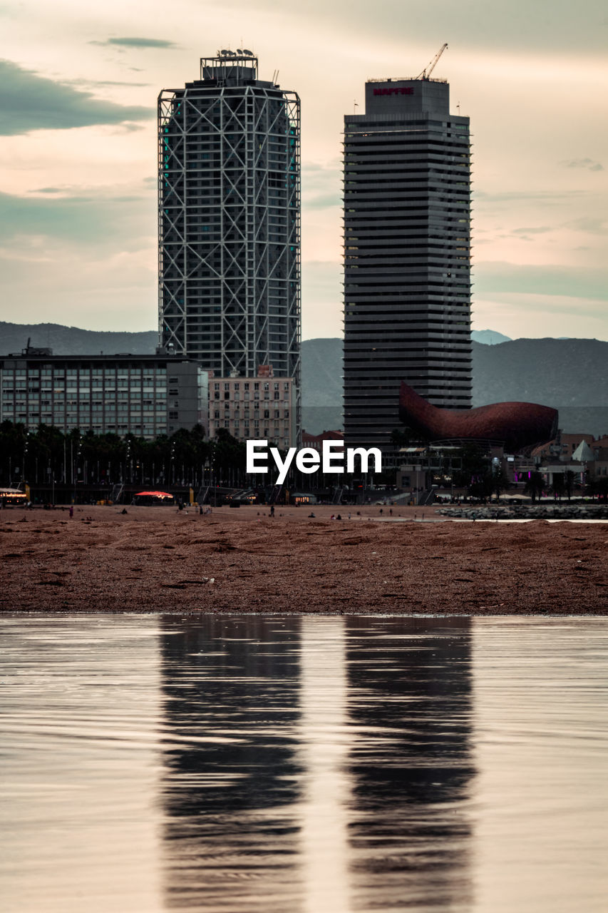Modern buildings by river against sky during sunset in city