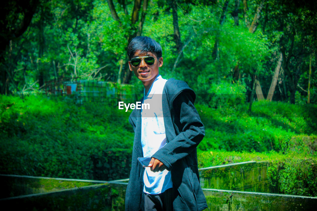 Portrait of smiling young man wearing sunglasses in forest