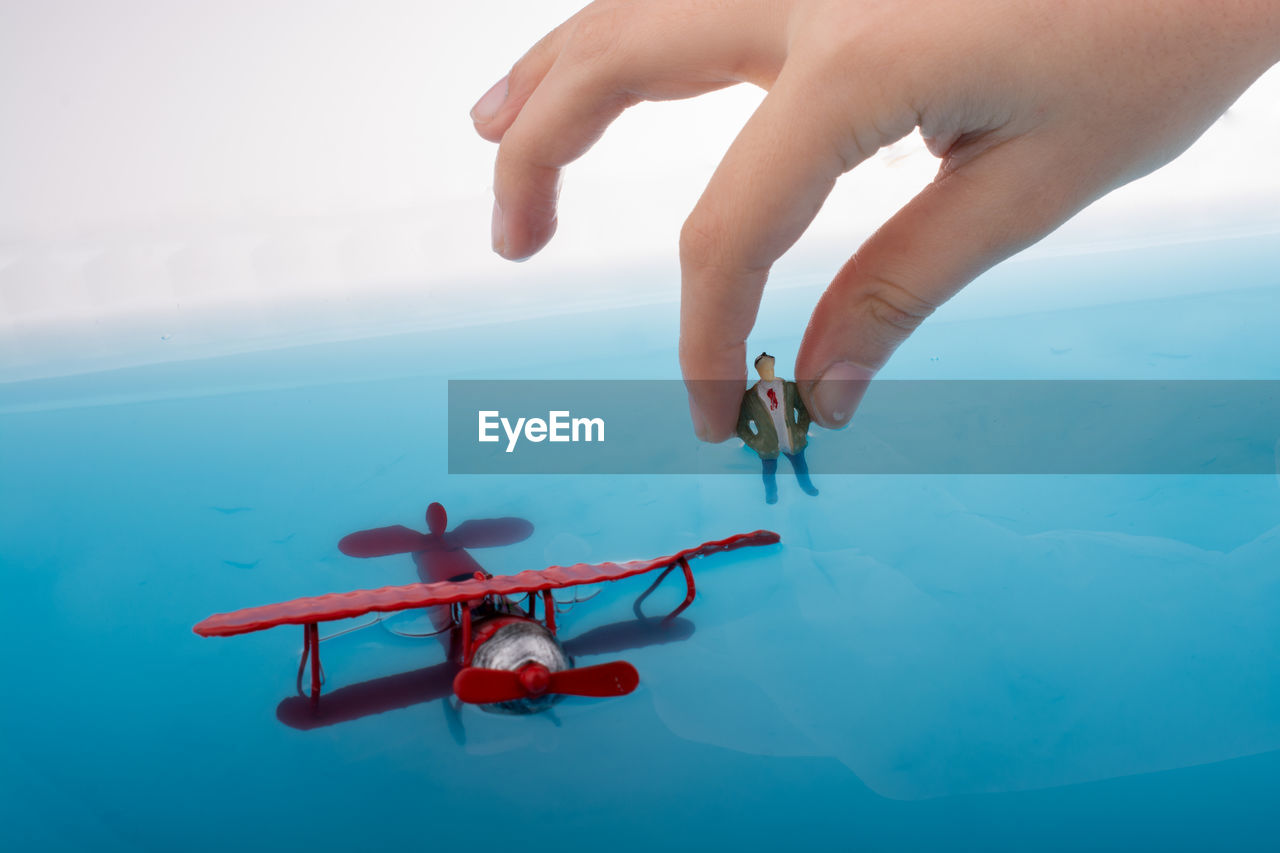 Close-up of person hand holding figurine by model airplane against sky