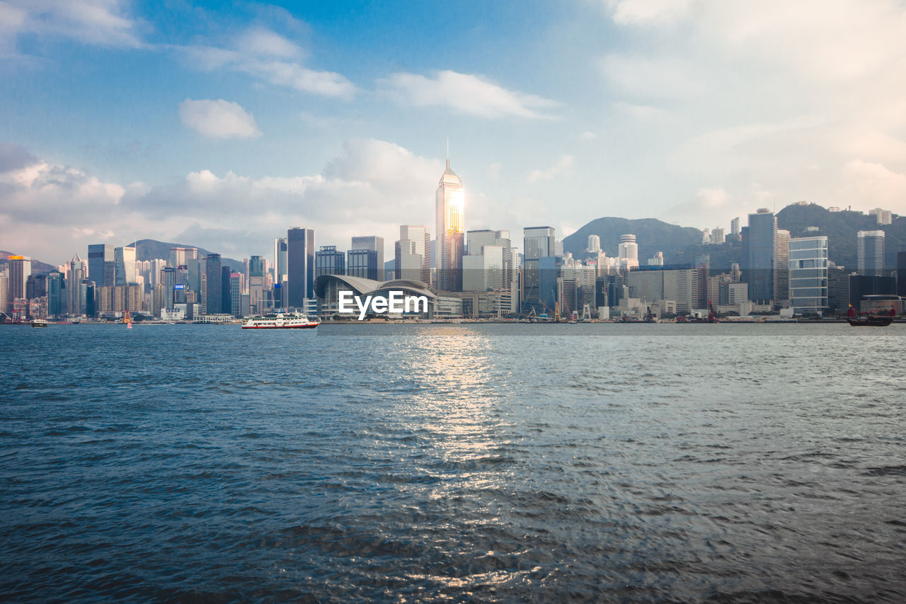 View of city at waterfront against cloudy sky