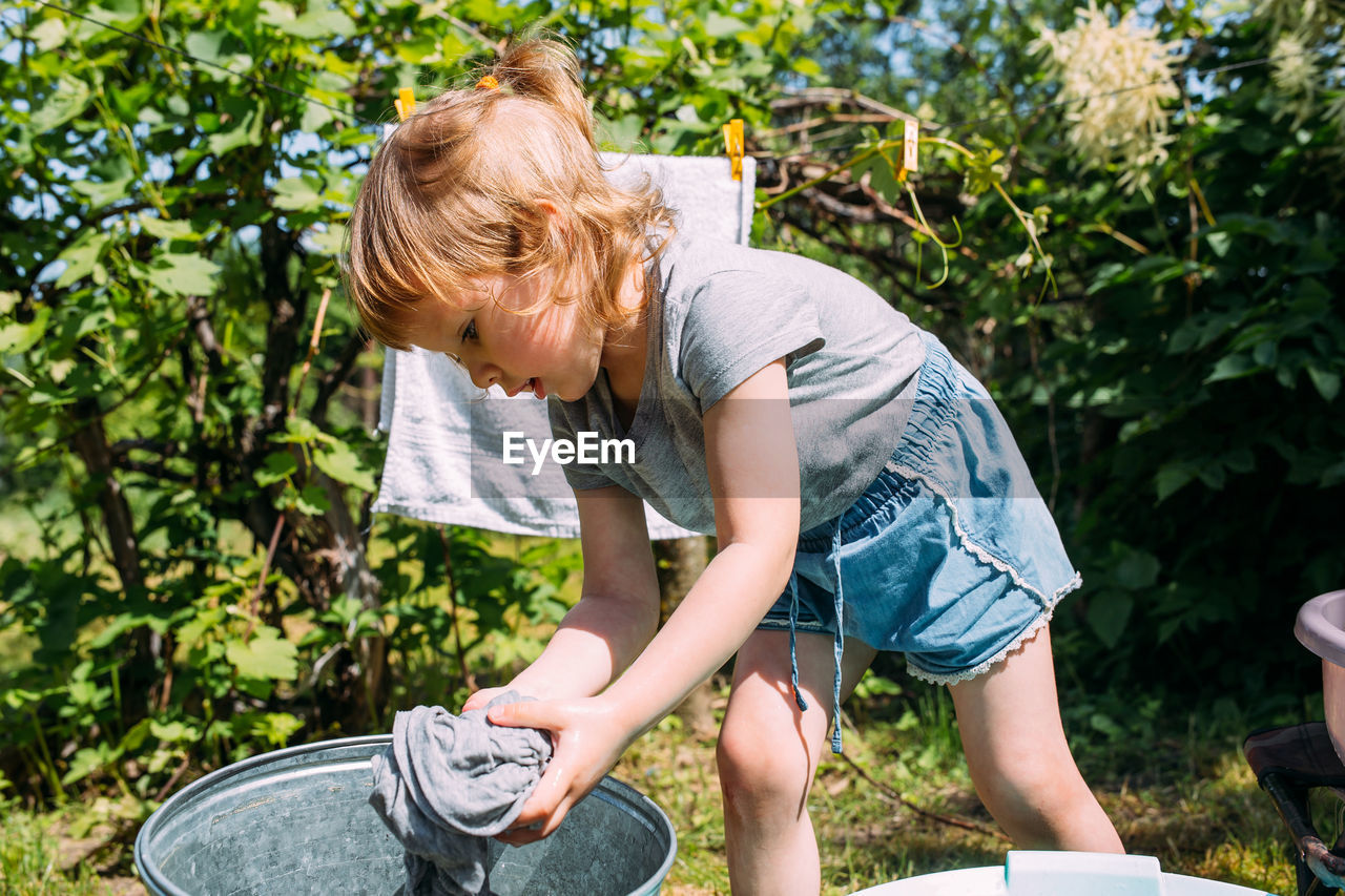 Little preschool girl helps with laundry. child washes clothes in garden