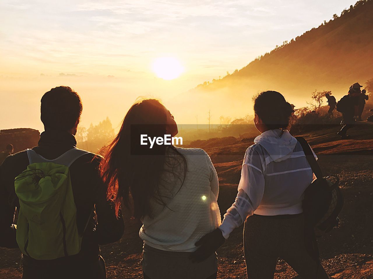 Rear view of people standing on landscape against sky during sunset