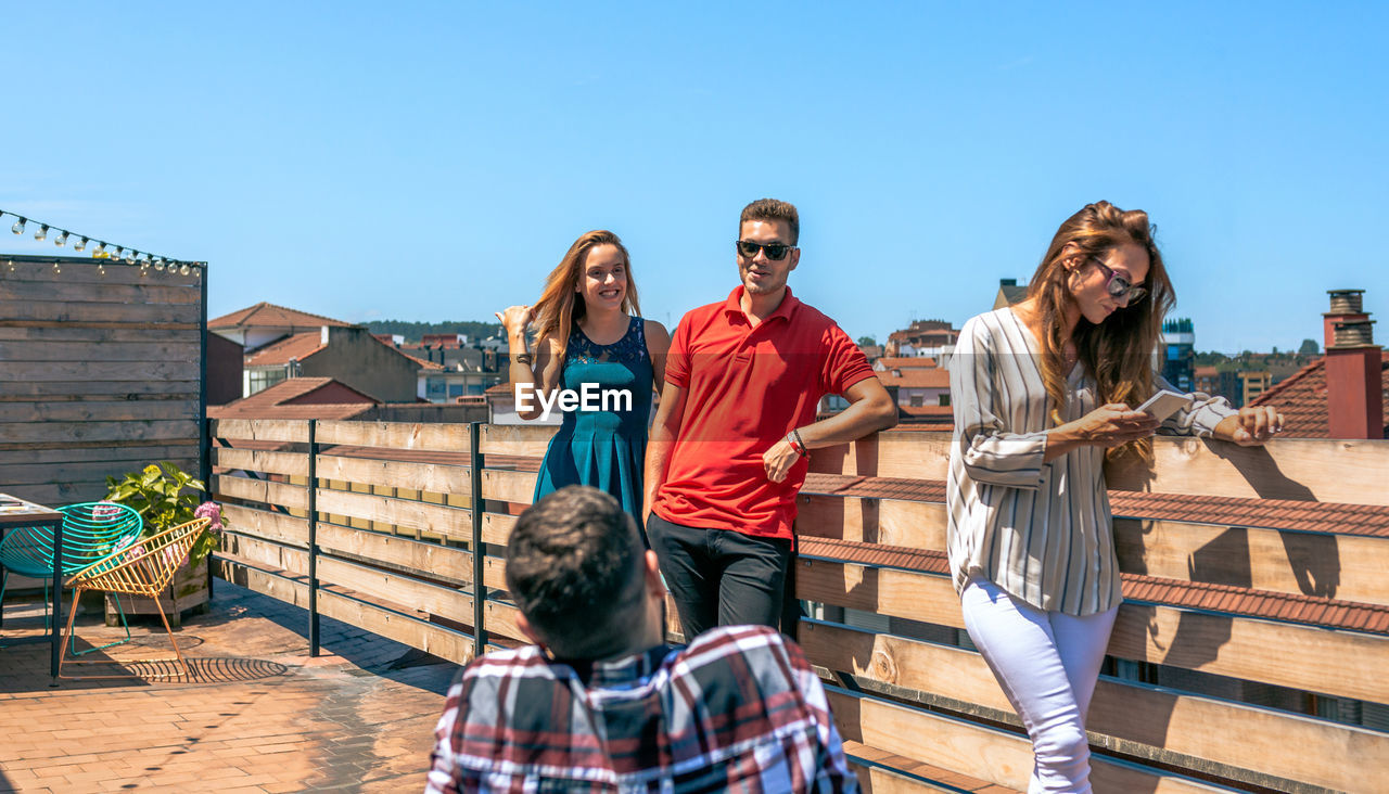 Happy friends talking in rooftop city while woman looking her phone