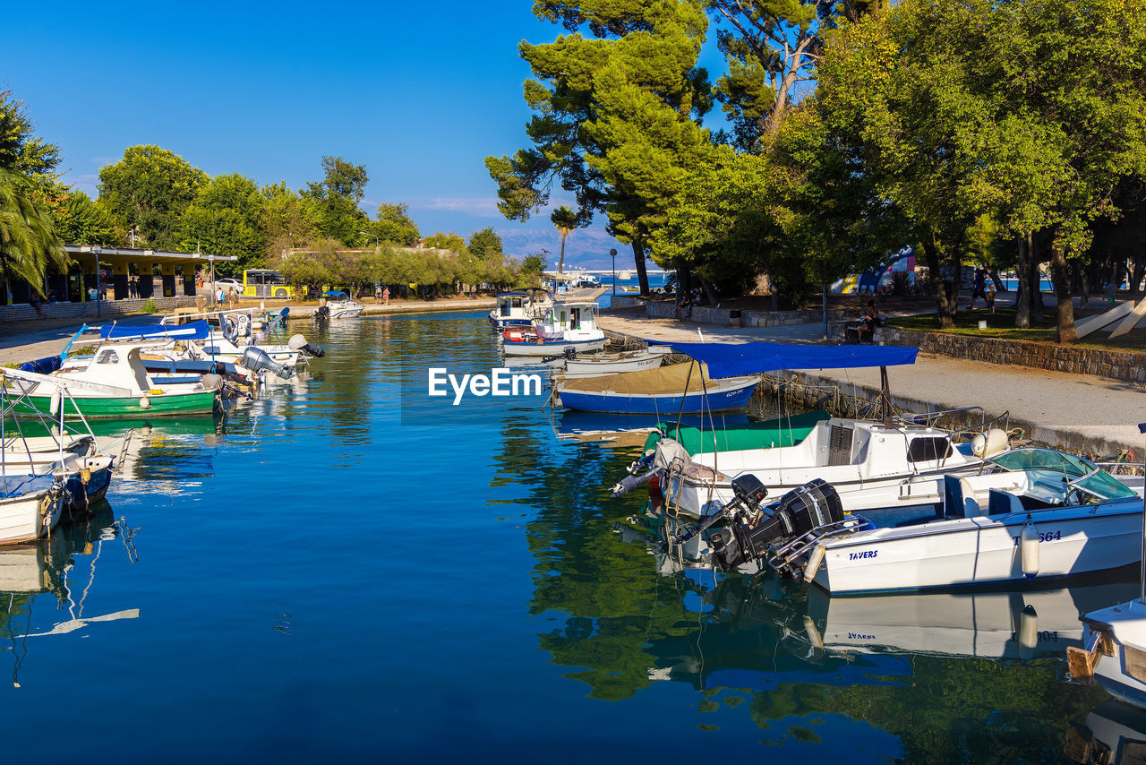 water, nautical vessel, tree, transportation, moored, mode of transportation, plant, nature, marina, boat, reflection, dock, harbor, vehicle, day, sky, travel, waterway, travel destinations, no people, body of water, lake, watercraft, architecture, tranquility, outdoors, blue, sunlight, beauty in nature, ship, land, tourism, vacation, boating, holiday, clear sky, trip, waterfront, pier, recreational boat, beach, sunny, scenics - nature, yacht, summer, building exterior, tranquil scene, built structure, city, idyllic